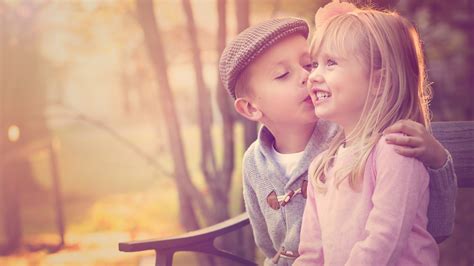 Cute Little Boy Is Kissing A Smiley Girl Sitting On Wooden