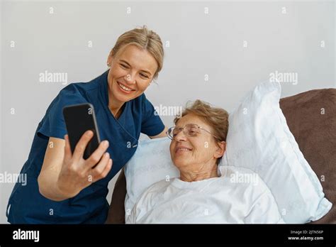 Doctor Or Nurse Caring For An Elderly Woman With A Mobile Phone Takes A