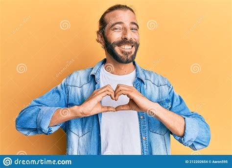 Attractive Man With Long Hair And Beard Wearing Casual Denim Jacket Smiling In Love Doing Heart