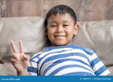 Asian Little Boy Sit On Sofa Holding Up The Peace Sign Stock Image