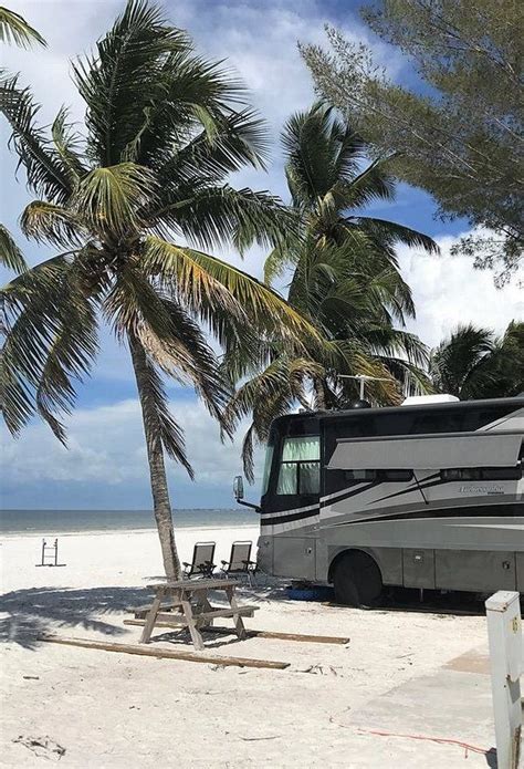 An Rv Parked On The Beach Next To A Palm Tree And Picnic Table With Chairs