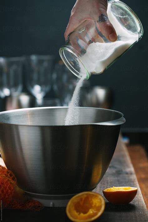 Womans Hand Pouring Caster Sugar Into A Mixing Bowl From A Glass Jar