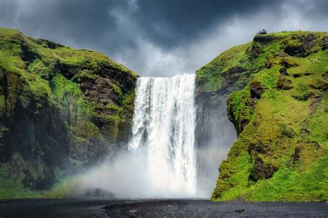 Majestic Skogafoss Waterfall Flowing With Rainbow And Moody Sky In