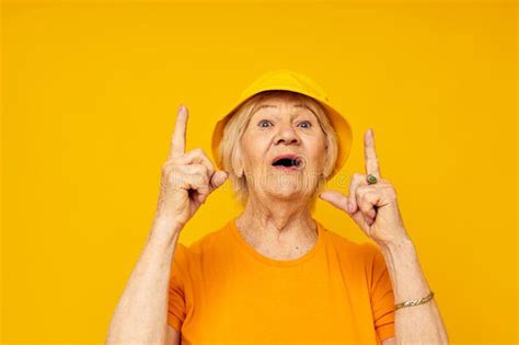 Portrait Of An Old Friendly Woman In Yellow T Shirts Hat Posing