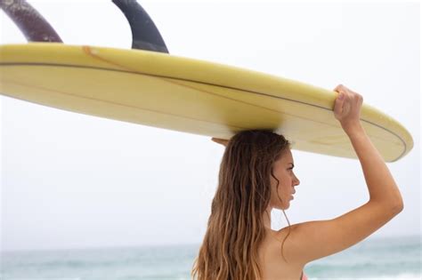 Premium Photo Female Surfer Carrying Surfboard On Her Head At Beach