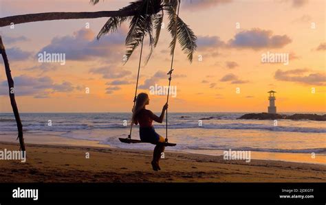 Silhouette Of Woman Sitting On Swing In Sea At Sunset Hi Res Stock