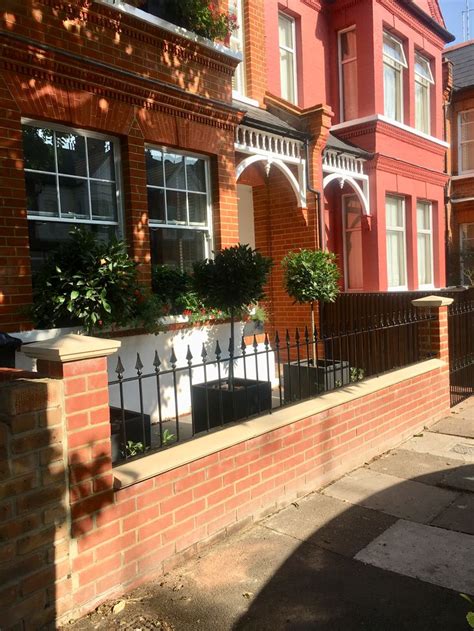 A Red Brick House With An Iron Fence And Planters On The Windowsills