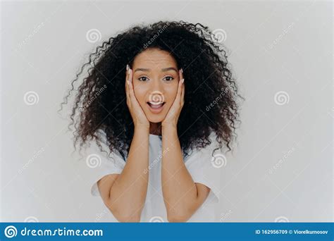Photo Of Surprised Cheerful Woman With Afro Haircut Keeps Both Hands On Cheeks Has Natural