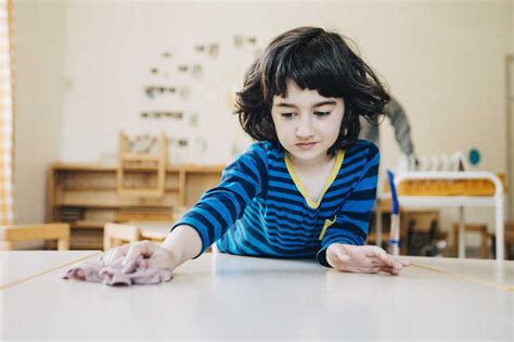 Boy Cleaning Table With Dish Cloth In Child Care Classroom Stock Photo