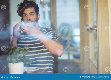 Man Sipping Coffee While Talking On Cellphone At Cafe Stock Photo