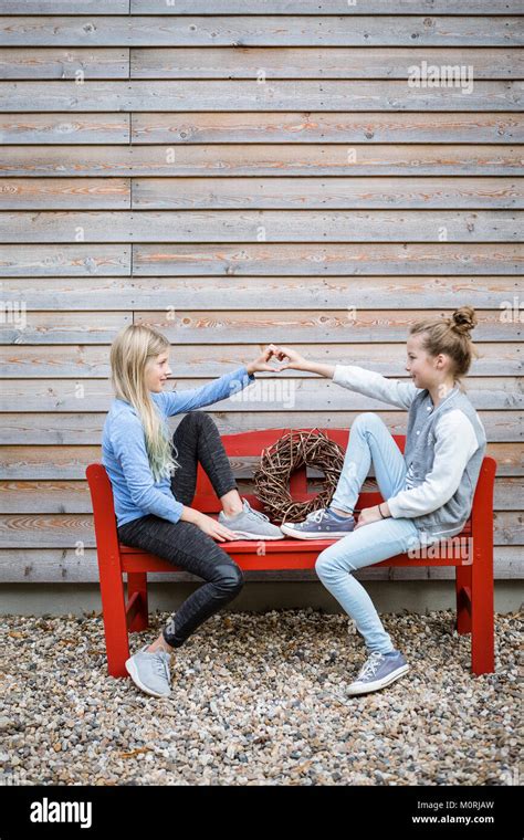 Two Best Friends Sitting On A Red Bench In Front Of A Wooden Facade