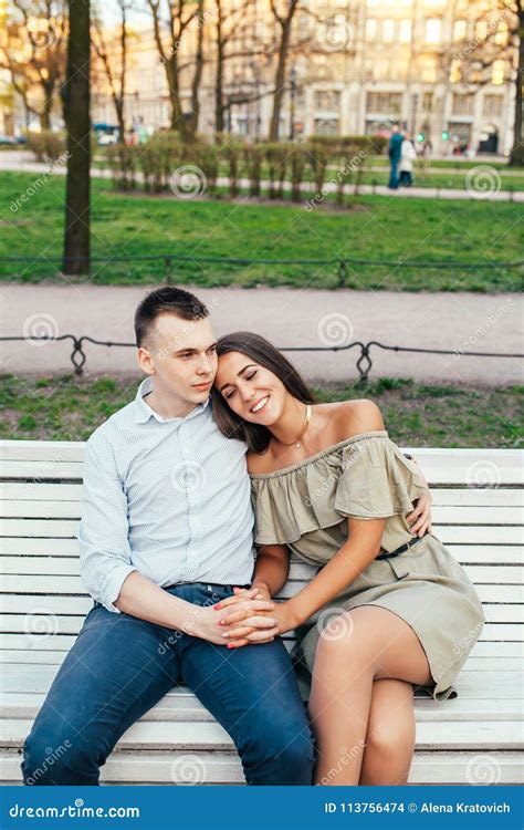 Happy Young Couple In Love Sitting On A Park Bench And Hugging Stock