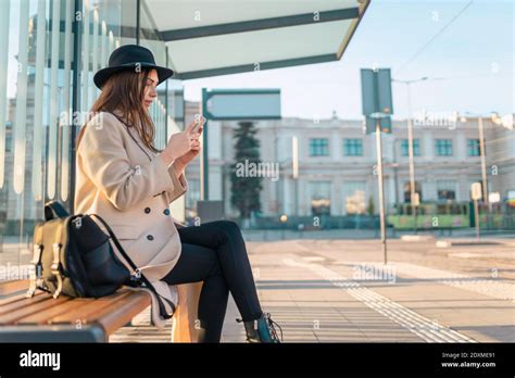 Tourist Girl Sits At Public Transport Stop And Looks In Smartphone