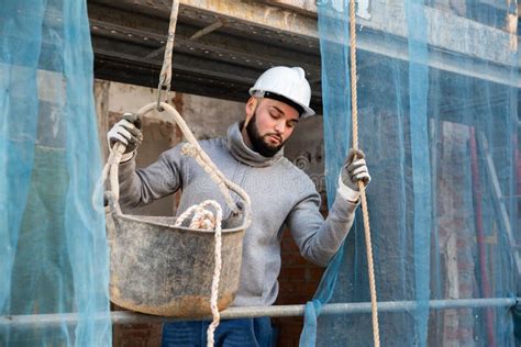Worker Lowering Down Bucket With Construction Mortar Stock Photo