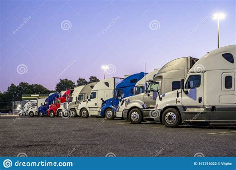 Different Big Rigs Semi Trucks Standing In Row On The Night Truck Stop