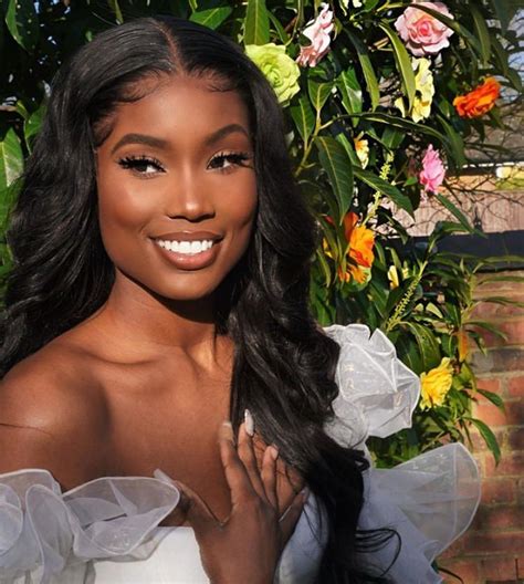 A Woman With Long Hair Wearing A White Dress And Posing In Front Of Some Flowers