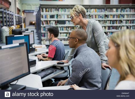 Librarian Helping College Student At Computer In Library Stock Photo