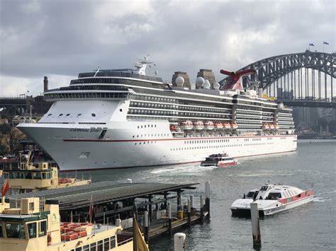 A Large Cruise Ship In The Water Next To A Dock With Boats On It And A Bridge In The Background