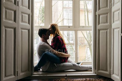Side View Of Young Couple Kissing On Window Sill At Home — Woman Man
