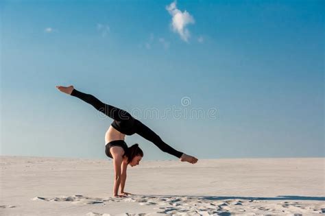 Young Woman Practicing Handstand On Beach With White Sand And Bright
