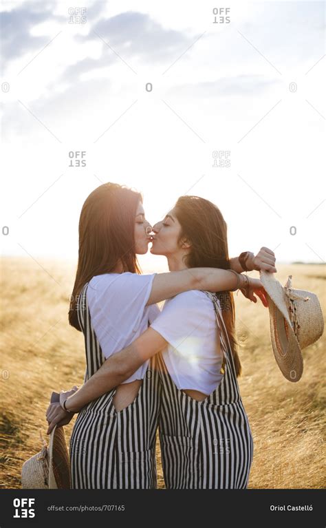 Side View Of Two Female Twins Hugging And Kissing In Wheat Field Stock