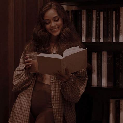 A Woman Is Reading A Book In Front Of A Bookshelf And Smiling At The Camera
