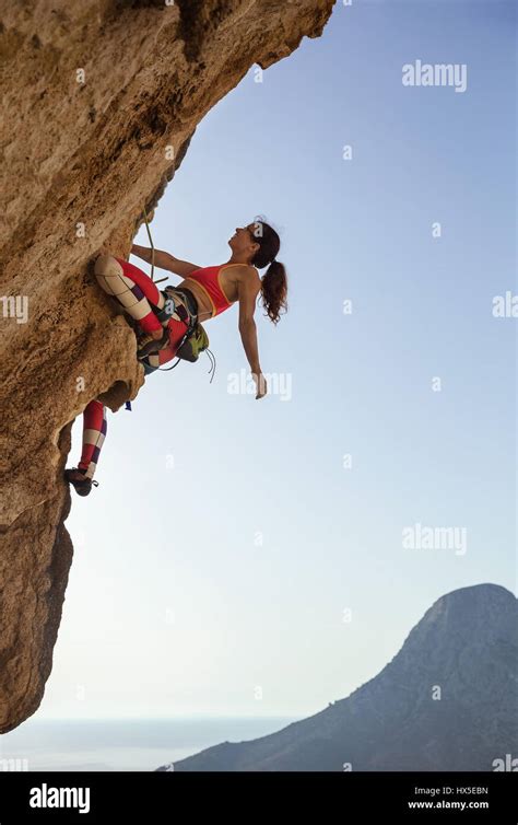 Female Rock Climber Looking Up At Challenging Route On Cliff And