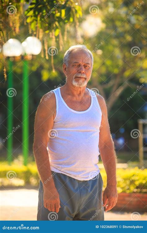 Grey Bearded Old Man In Vest Stands In Park By Street Lamps Stock Image