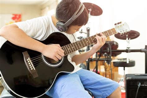 Niño Tocando Una Guitarra Acústica Con Auriculares En Foto Premium