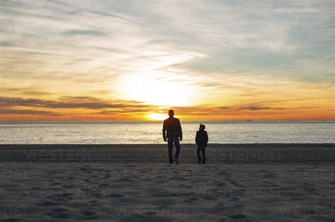 Father And Son Walking On The Beach At Sunset Stock Photo