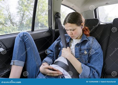 Teen Girl Sitting In Car In Back Passenger Seat With Smartphone And