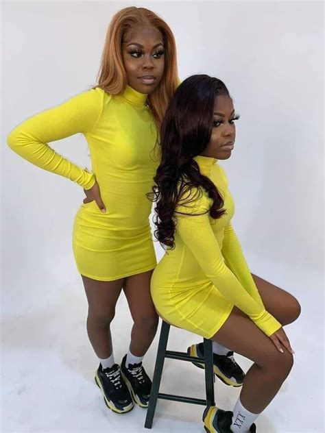 Two Women In Yellow Dresses Posing For The Camera One Is Sitting On A Stool