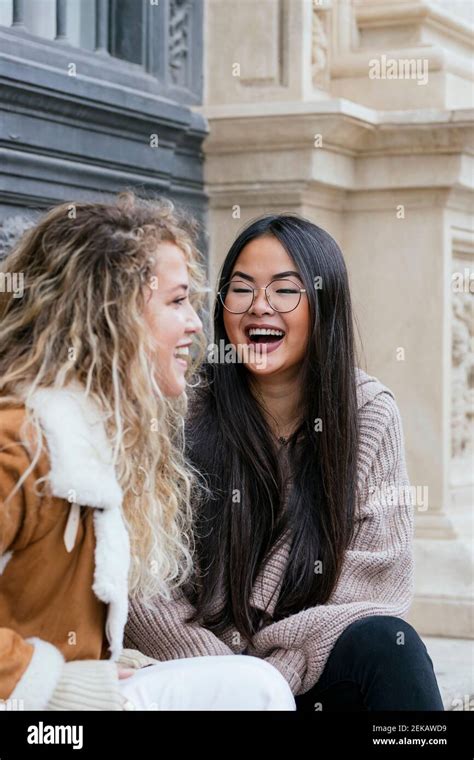 Female Friends Laughing While Sitting Outdoors Stock Photo Alamy