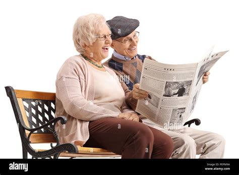 Senior Couple Seated On A Bench Reading A Newspaper And Laughing