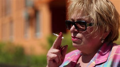 senior woman sits on the bench and smokes a cigarette blonde woman with a cigarette female