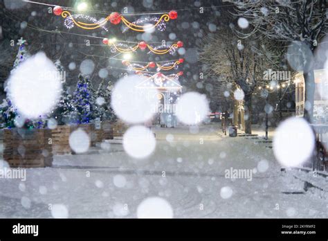 City Street During Snowfall At Winter Night Many Decorated Christmas