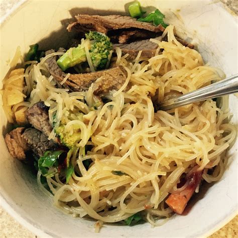 A White Bowl Filled With Noodles Meat And Broccoli On Top Of A Table