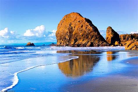 The Beach Is Covered In Blue Water And Sand With Large Rocks Sticking