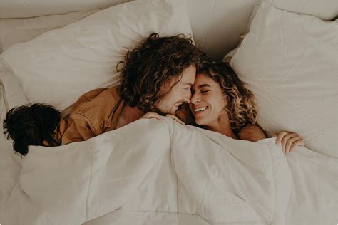 A Man And Woman Laying In Bed Under The Covers
