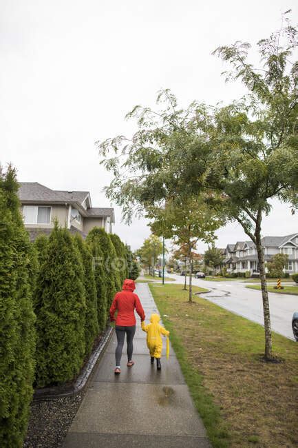 Rear View Of Mother Walking With Toddler Child On The Sidewalk — House