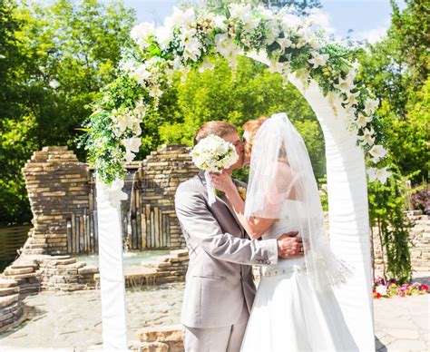 First Kiss Of Newly Married Couple Under Wedding Arch Stock Photo