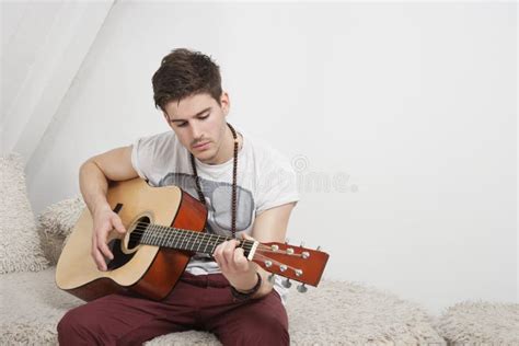 Young Caucasian Man Playing Guitar While Sitting On Fur Sofa Stock
