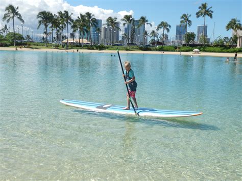 A Person On A Surfboard In The Water With Palm Trees And Buildings In