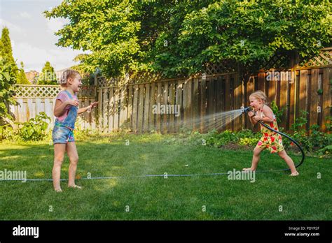 Two Girls Splashing Each Other With Gardening House On Backyard On
