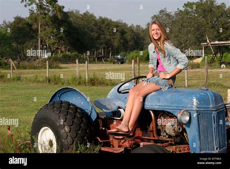 A Beautiful Blond Girl Sitting On A Tractor In The Middle Of A Farm