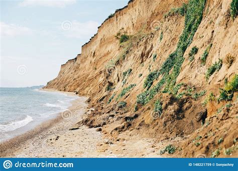 Beautiful Sandy Cliff With Grass And Sea Waves On Beach