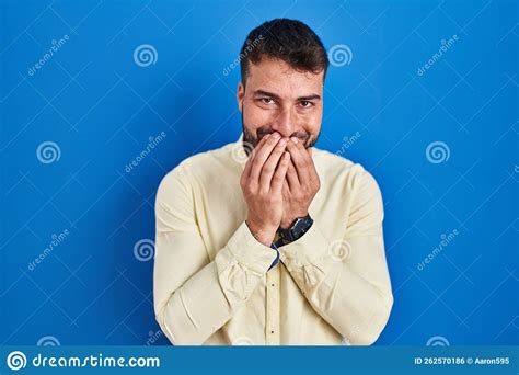 Handsome Hispanic Man Standing Over Blue Background Laughing And Embarrassed Giggle Covering