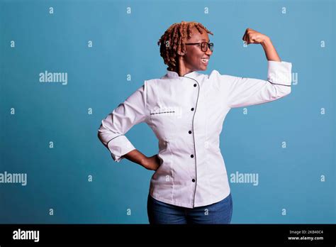 Female kitchen staff member wearing chef jacket smiling as looks at arm