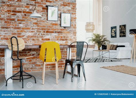 Chairs At Table Against Red Brick Wall With Posters In Modern Apartment