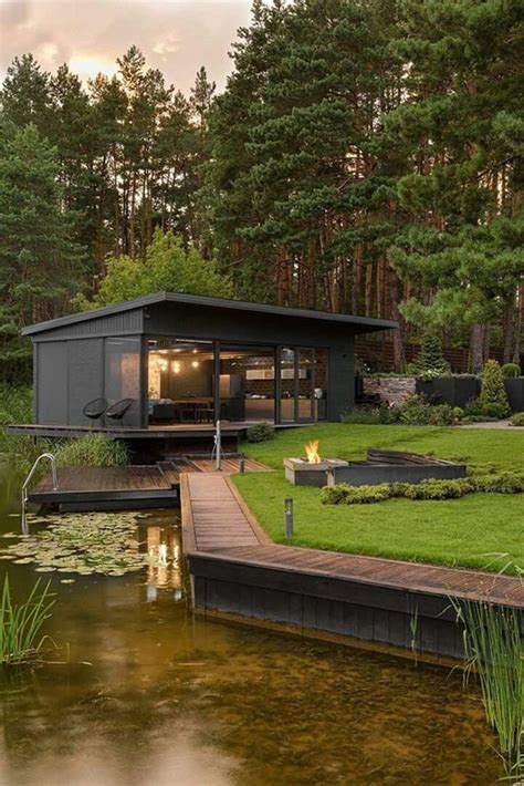 A House Sitting On Top Of A Lush Green Field Next To A Lake And Forest
